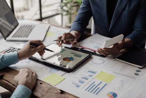 Two business professionals reviewing financial reports, charts, and a tablet displaying analytics, discussing financing options for small businesses