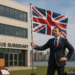 British businessman in front of US Subsidiary building holding UK flag, New York skyline in background