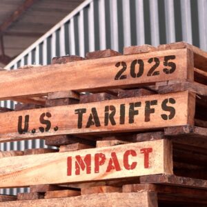 tacked wooden pallets marked with “2025 U.S. Tariffs Impact” outside a warehouse, symbolizing rising costs and supply chain pressure for small businesses