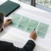 An anonymous finance leader compares four translucent green scenario sheets across a debt-planning grid in a bright boardroom.