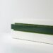 A low stack of three fitted stone courses on a bright white floor: a white base, a deep green middle course that projects slightly beyond the layers above and below, and a white top course, with thin bright green bands at the joints.